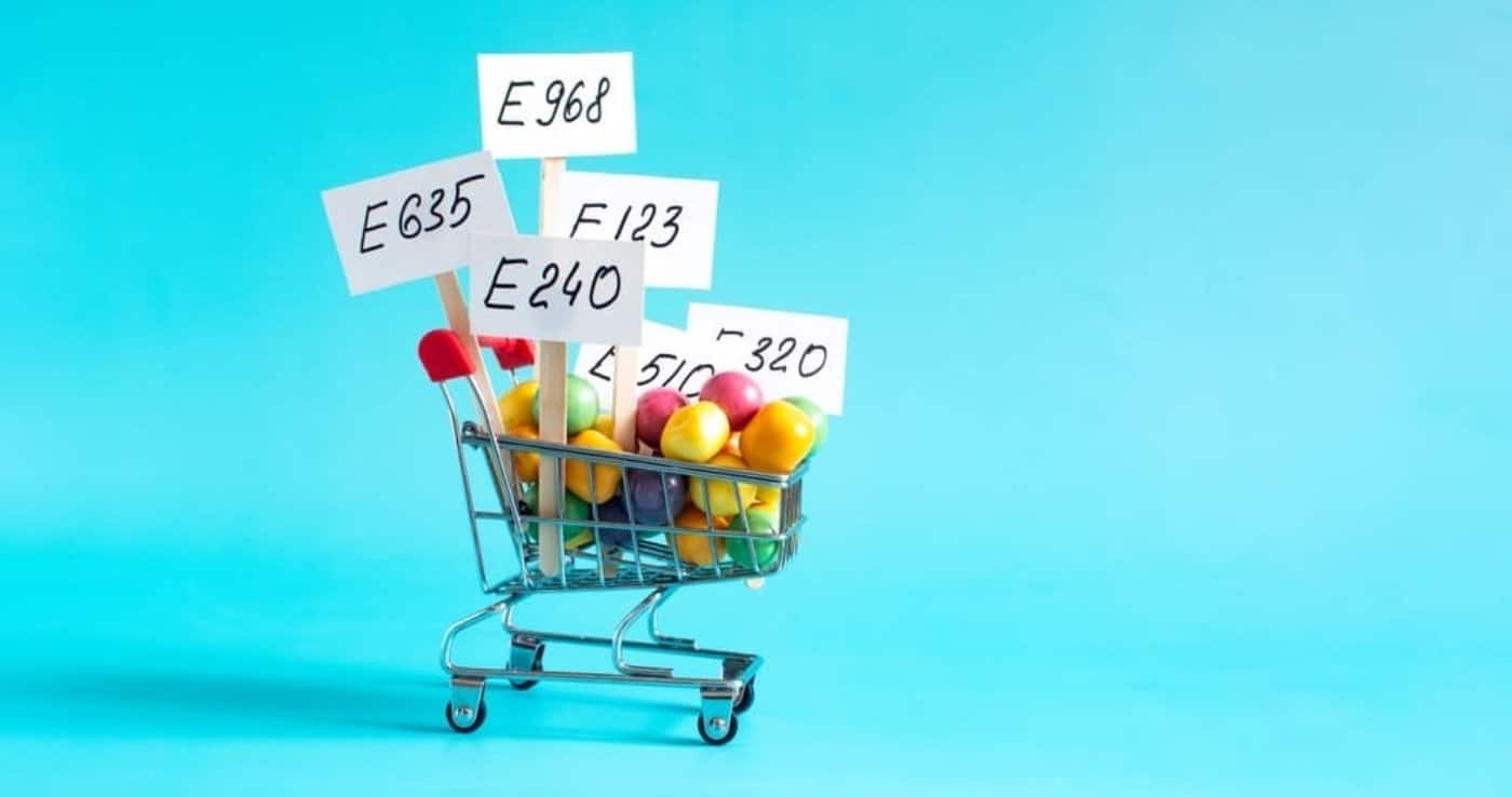 Carrito de la compra con carteles de números E de aditivos alimentarios sobre fondo azul