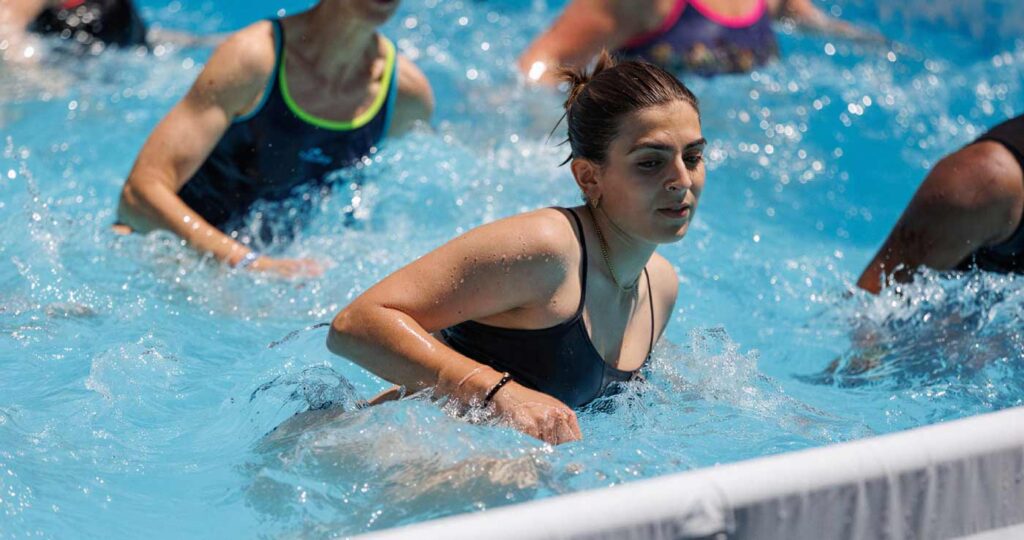 Mujeres jóvenes realizando movimientos energéticos aeróbicos en una piscina, creando salpicaduras