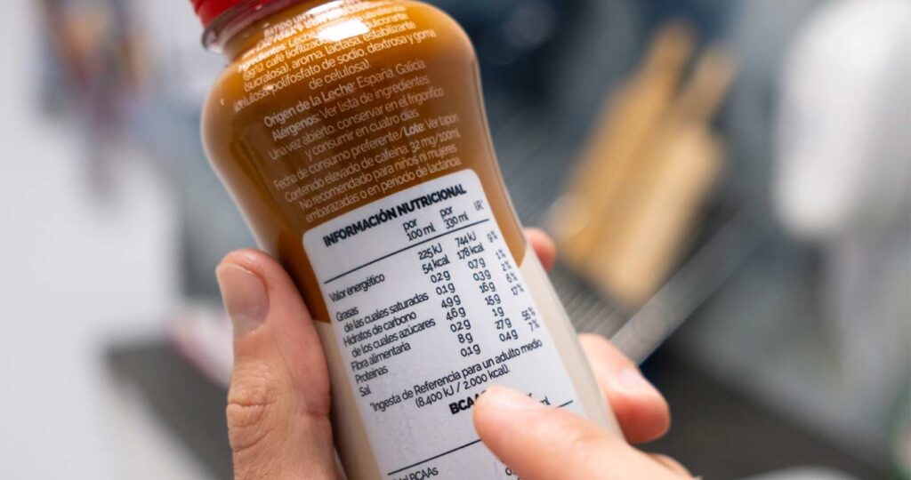 Mano sujetando un batido de optimilk señalando la etiqueta con valores nutricionales
