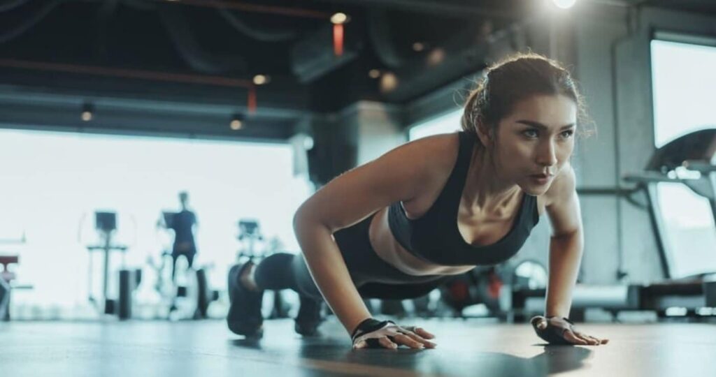 Mujer haciendo flexiones en el suelo del gimnasio durante un entrenamiento HIIT de alta intensidad