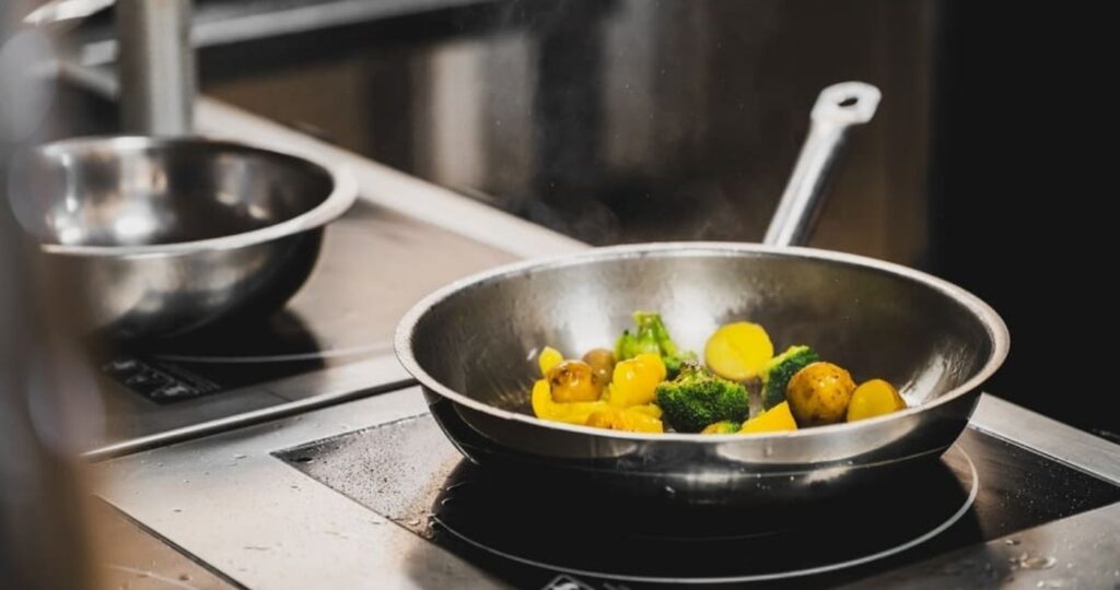 Sartén de acero inoxidable salteando brócoli y patatas sobre una placa de inducción