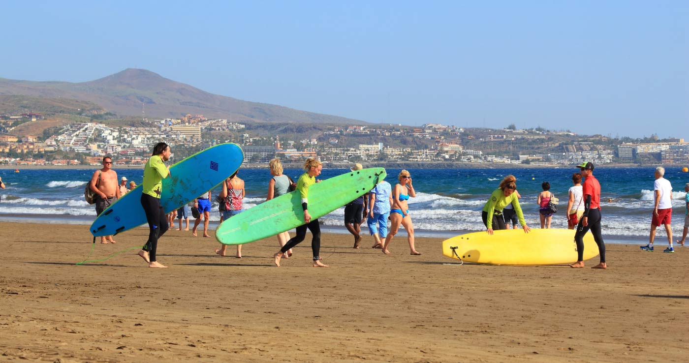 Personas con la tabla de surf yendo al agua en la Playa del Inglés
